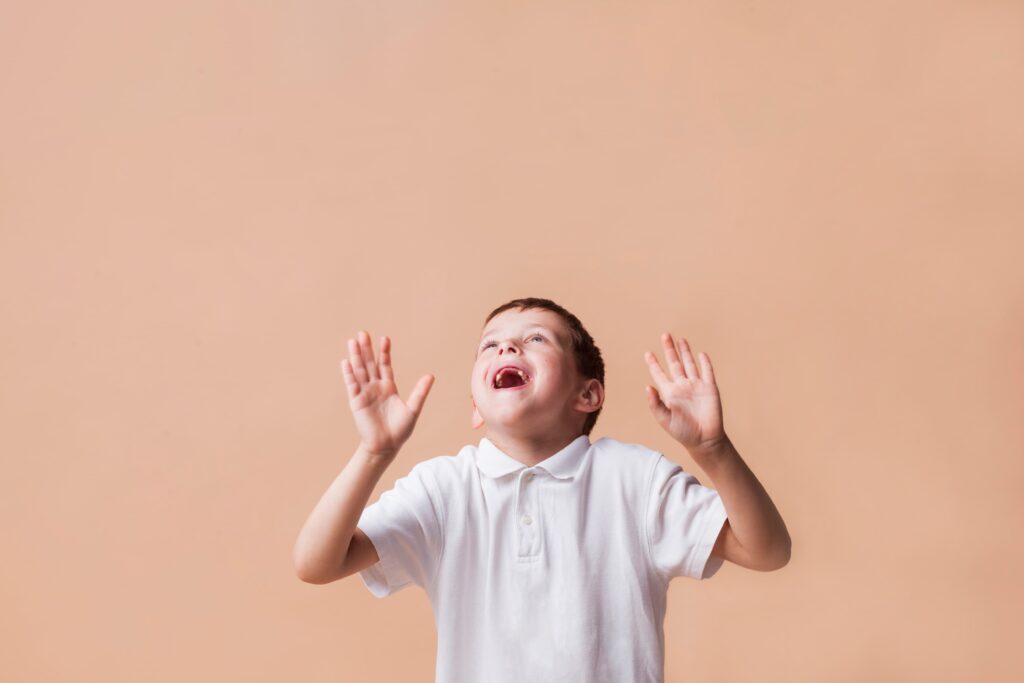 laughing boy looking up with hand gesturing beige background 1