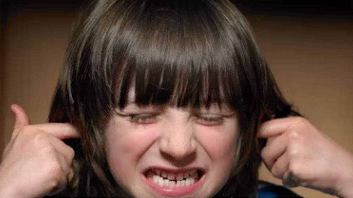 A young boy with a pained expression covers his ears, illustrating sound sensitivity commonly experienced by children with autism.