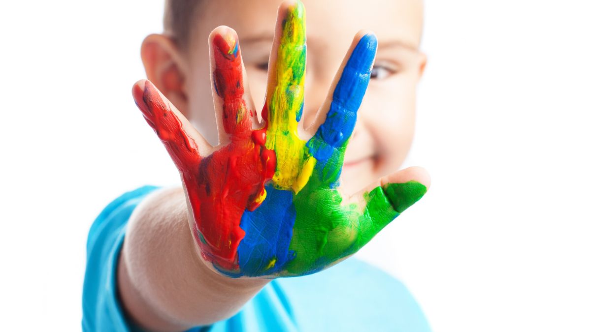 A child holds out their hands covered in multicolored paint toward the camera, symbolizing creativity and self-expression.