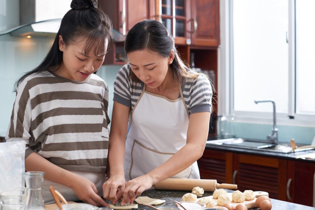 two young asian women cutting out cookies from dough kitchen counter 1