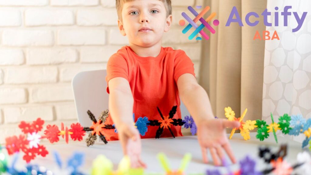 A young boy arranges flower-shaped puzzle pieces on a table and confidently presents his finished work, symbolizing Everyday Is Autism Awareness Day.