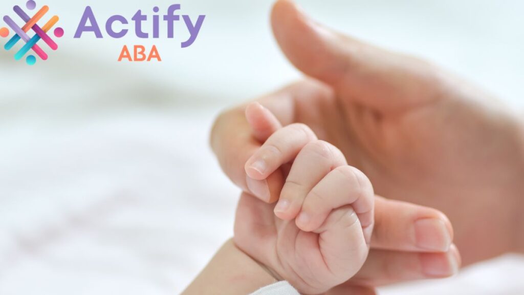 A baby’s hand is held by a parent in a bright, softly lit room, illustrating autism brain differences.