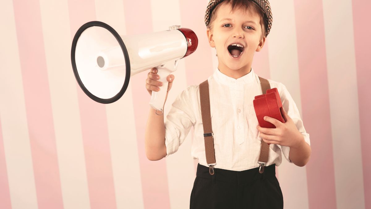 Speech goals for autism: a boy wearing a bowtie stands against a pink striped background, holding a megaphone while announcing something.